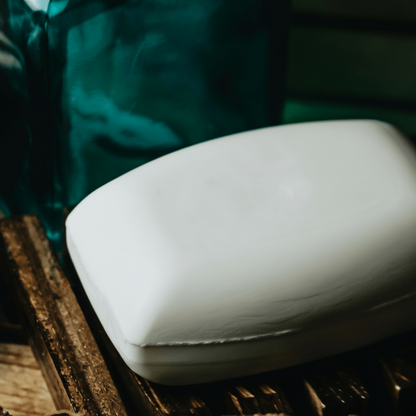 White bar of soap on a wooden surface with a blurred green background